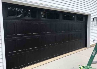 Black panel style garage door on a white house.