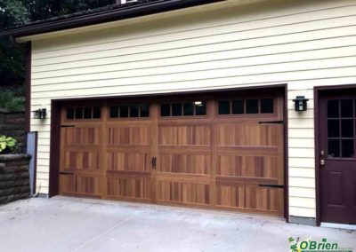 Carriage Style wooden Garage Door on white panel house.