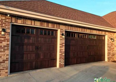 Dark oak carriage-style garage door on tan brick house.