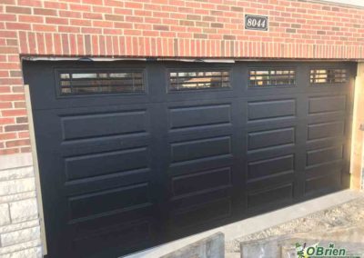Black panel garage door with windows on brick house.