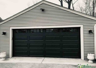 Black panel garage door with windows on gray house.