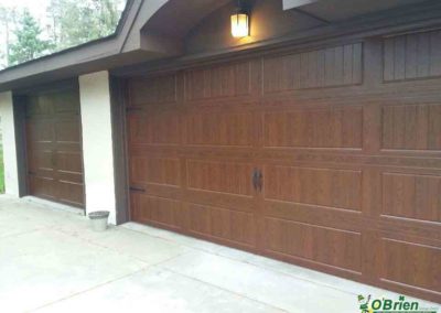 Dark oak carriage-style garage door on gray and white house.