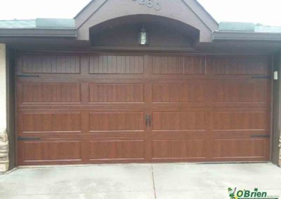 Dark oak carriage-style garage door on gray and white house.